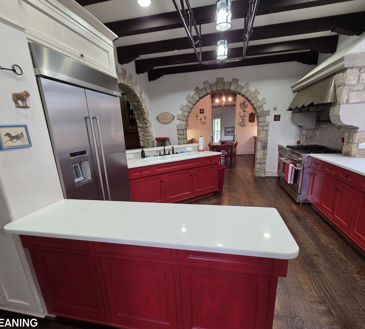 A spotless Spanish-style kitchen with red cabinetry, stone archway, wood beam ceiling and stainless steel appliances.